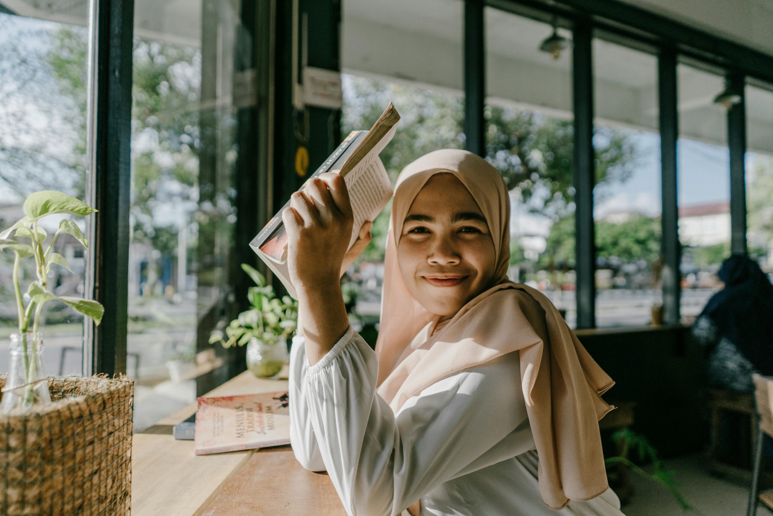 Smiling Hijab Girl Enjoying a Book in a Cozy Coffee Shop in the City